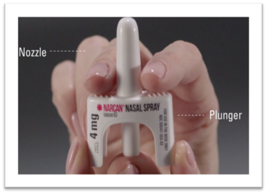 A person's hands hold a white Narcan nasal spray device. The device is labeled